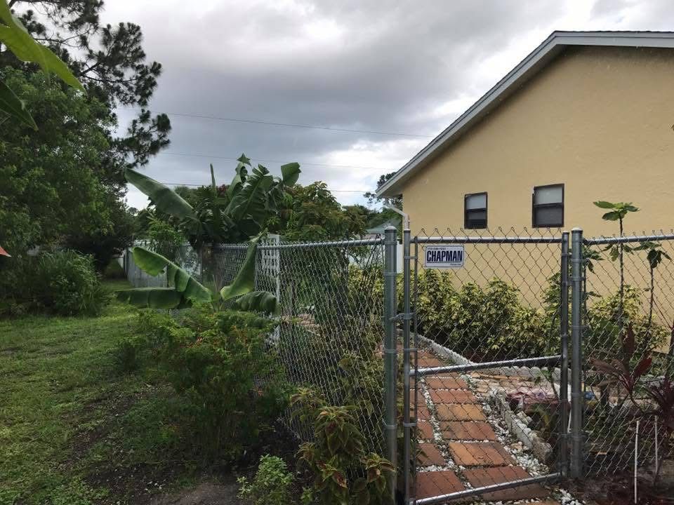 A chain link fence surrounds a brick walkway leading to a house