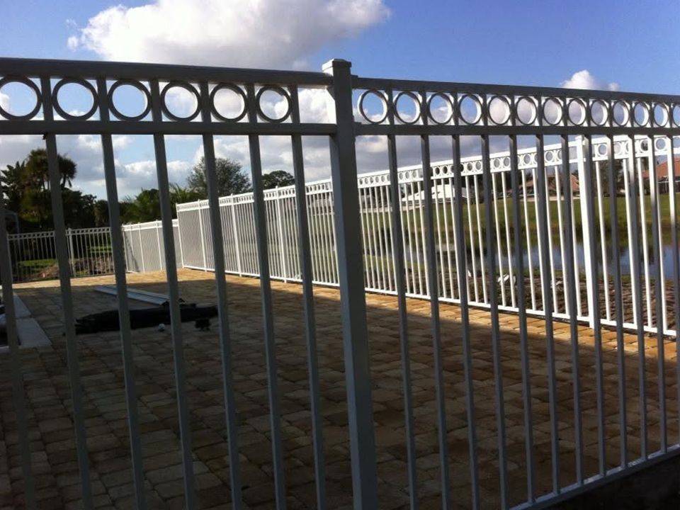 A white fence surrounds a sandy area near a body of water
