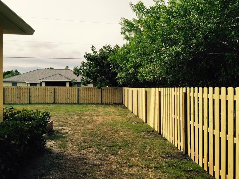 A wooden fence surrounds a grassy yard in front of a house