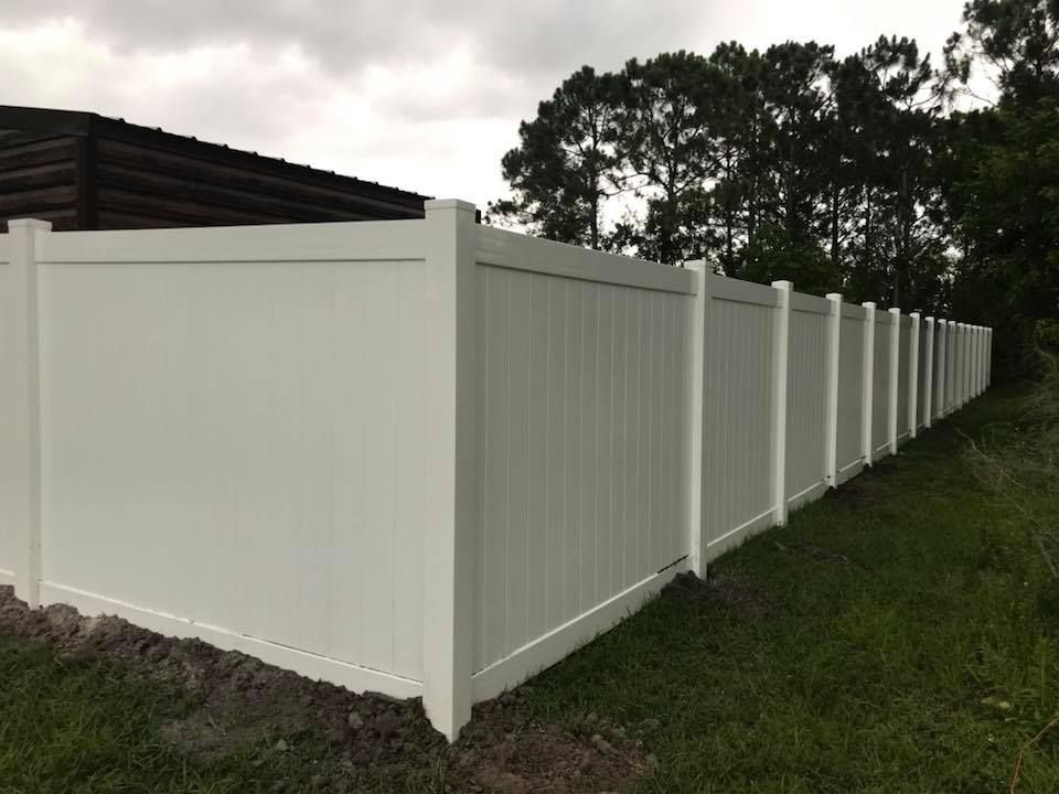 A white vinyl fence is surrounded by grass and trees.
