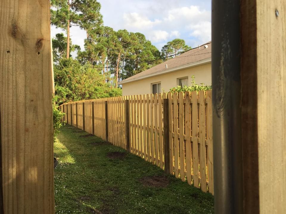 A wooden fence surrounds a lush green yard in front of a house.