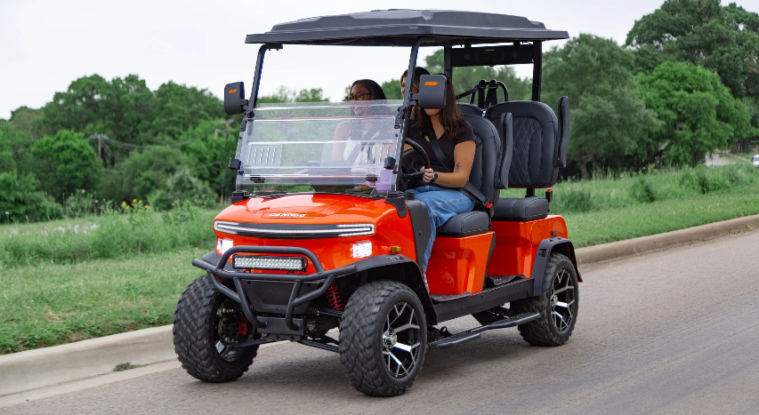 Rover XL: An orange golf cart with two people driving on a road lined with trees.