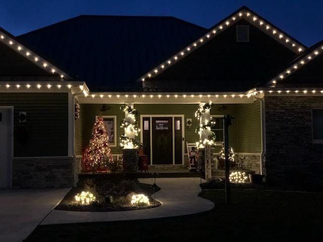 House with festive white holiday lights glowing at dusk, decorated front entry and yard shrubs