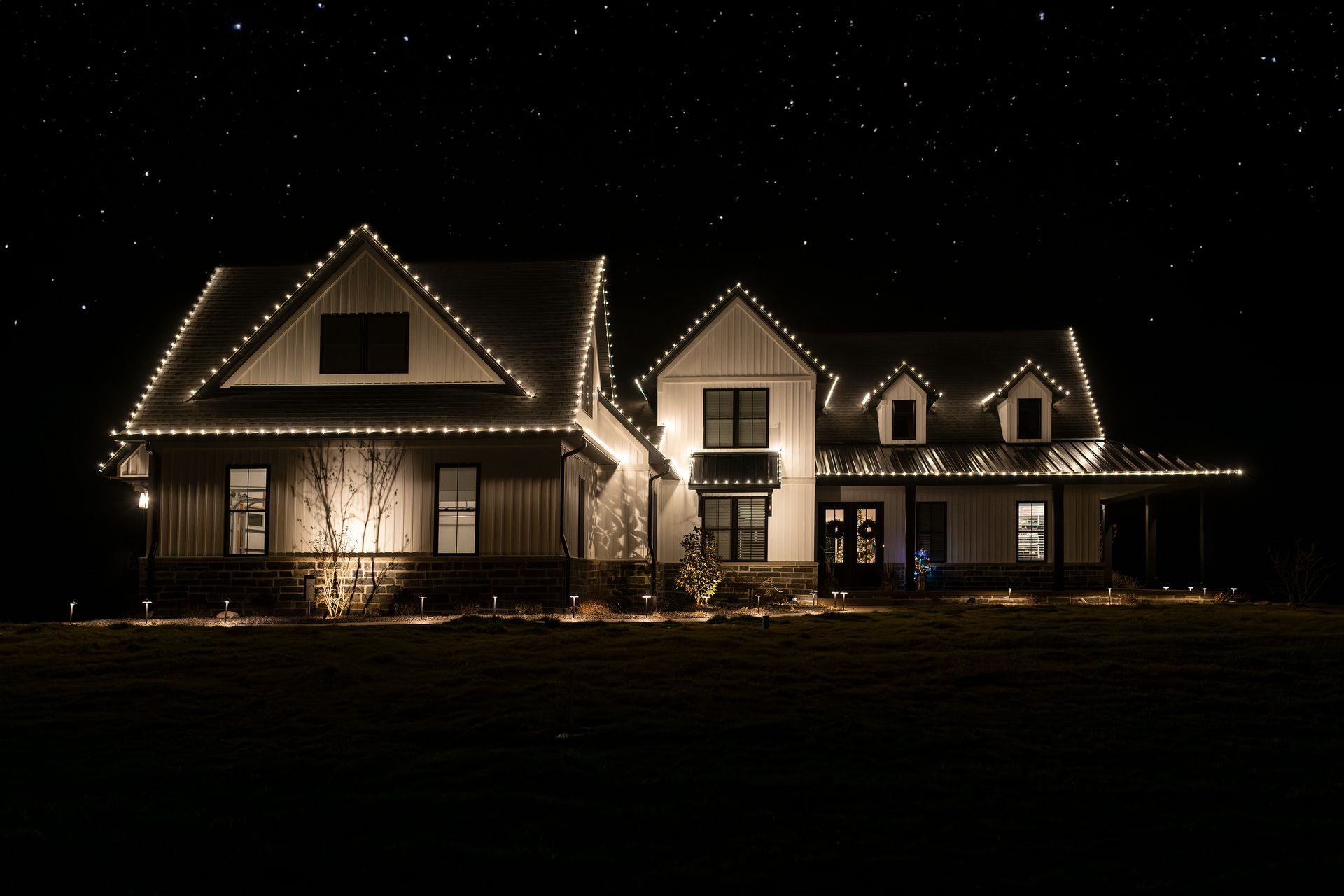 Large house outlined with warm white lights at night under a dark, starry sky