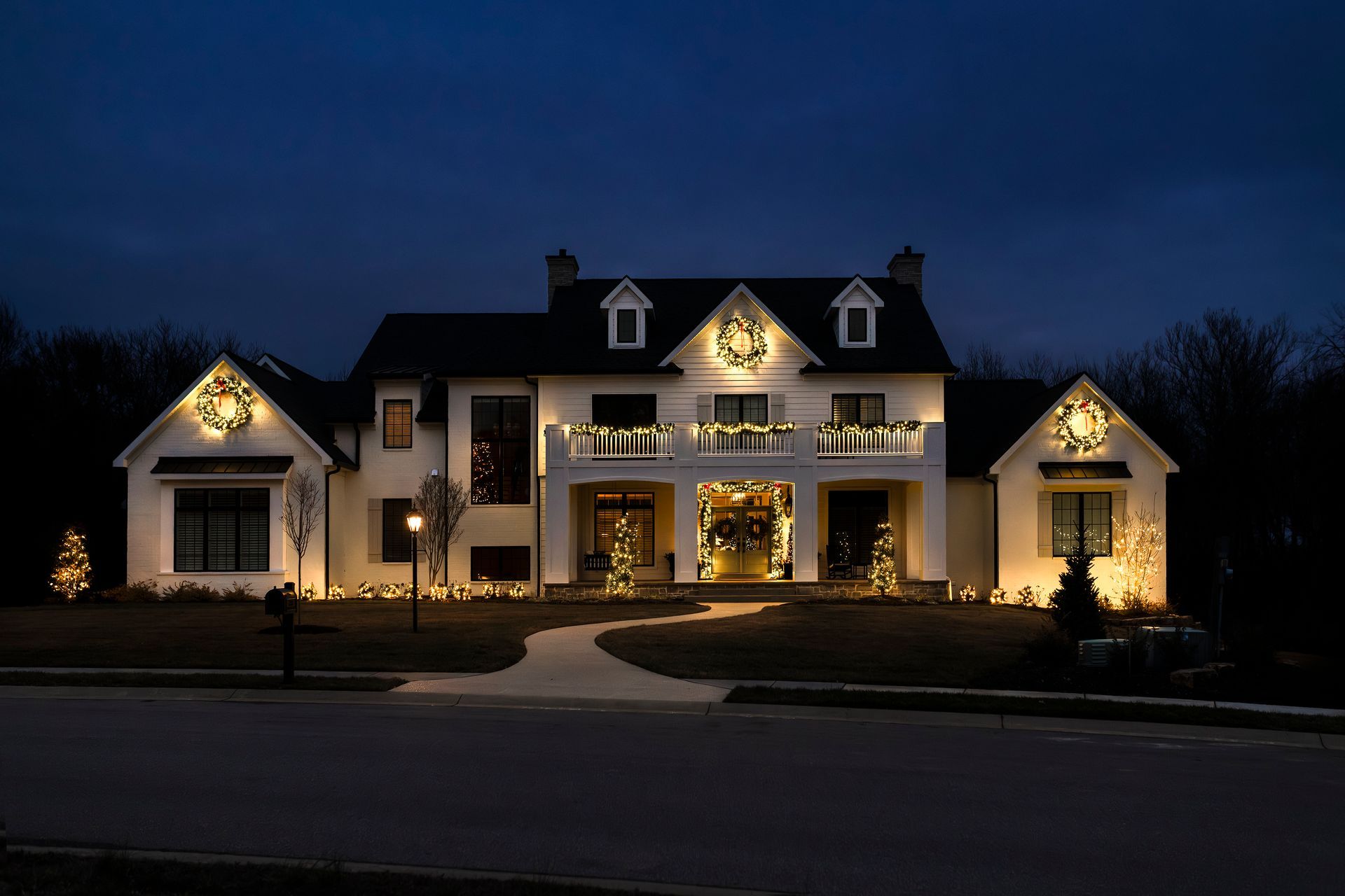 Large illuminated house at night with warm holiday lights and a curved driveway