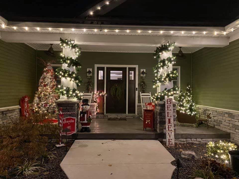 Holiday-decorated front porch with Christmas lights, wreaths, and red signs at night