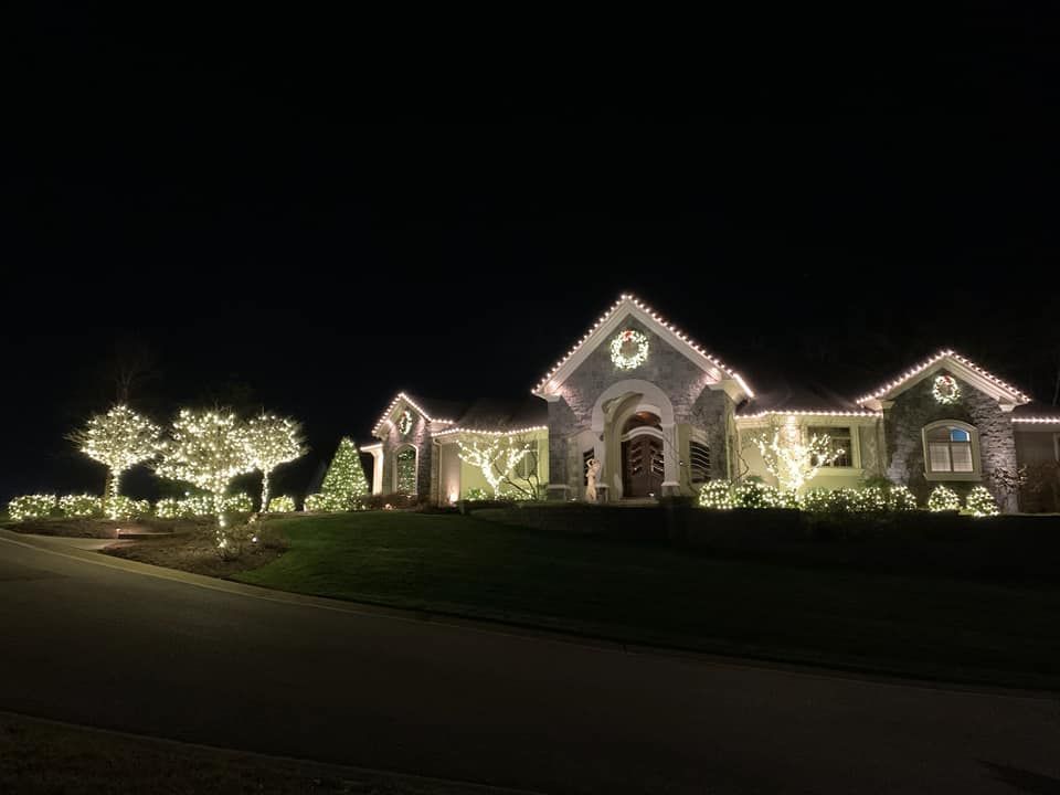 House decorated with white holiday lights at night, with lit trees and a dark lawn.