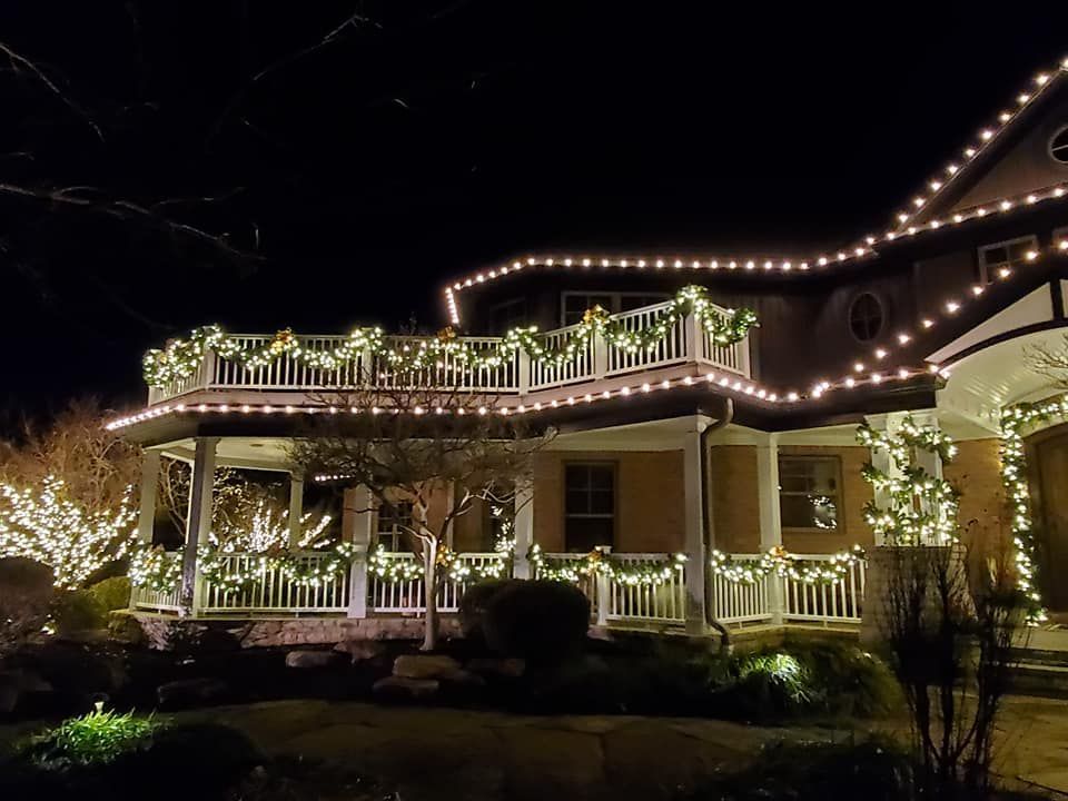 Lit-up Victorian house at night with white holiday lights and decorated wraparound porch