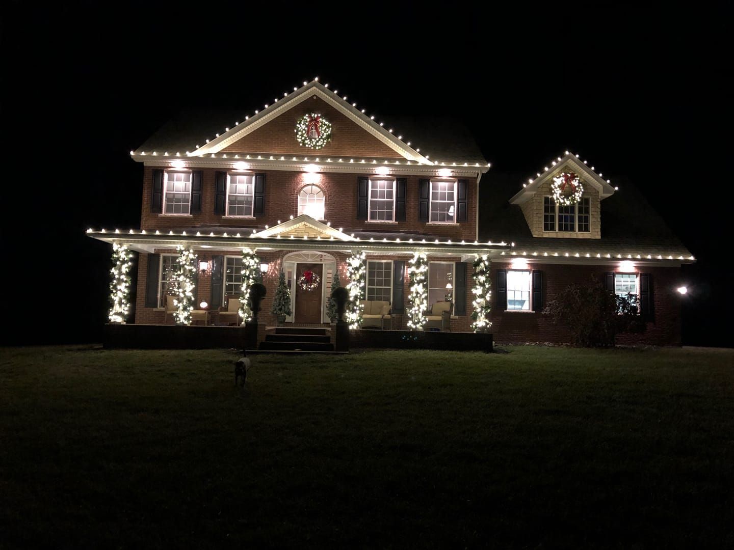A house lit with Christmas lights at night, glowing against a dark yard.