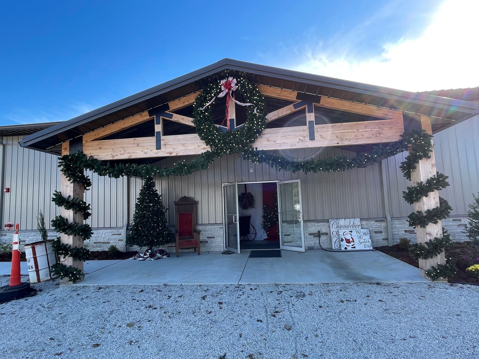 Decorated house entrance with Christmas wreaths, garlands, and a gravel driveway under a bright sky