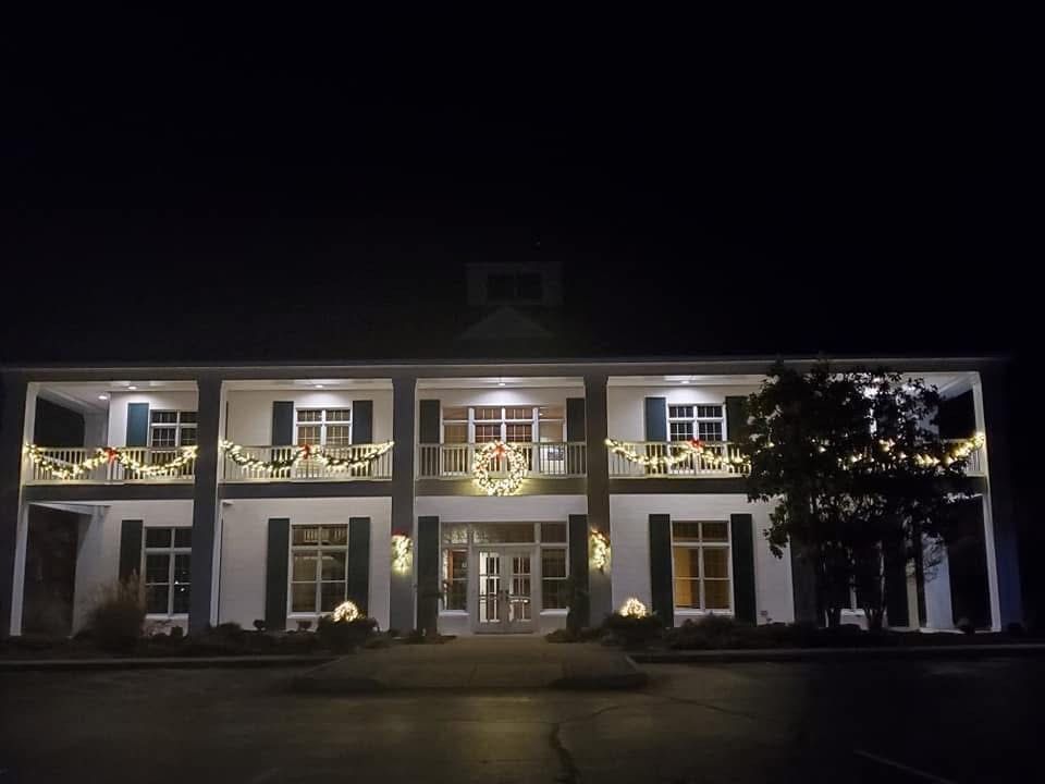 A lit two-story building at night with white columns and balconies, viewed from the front.