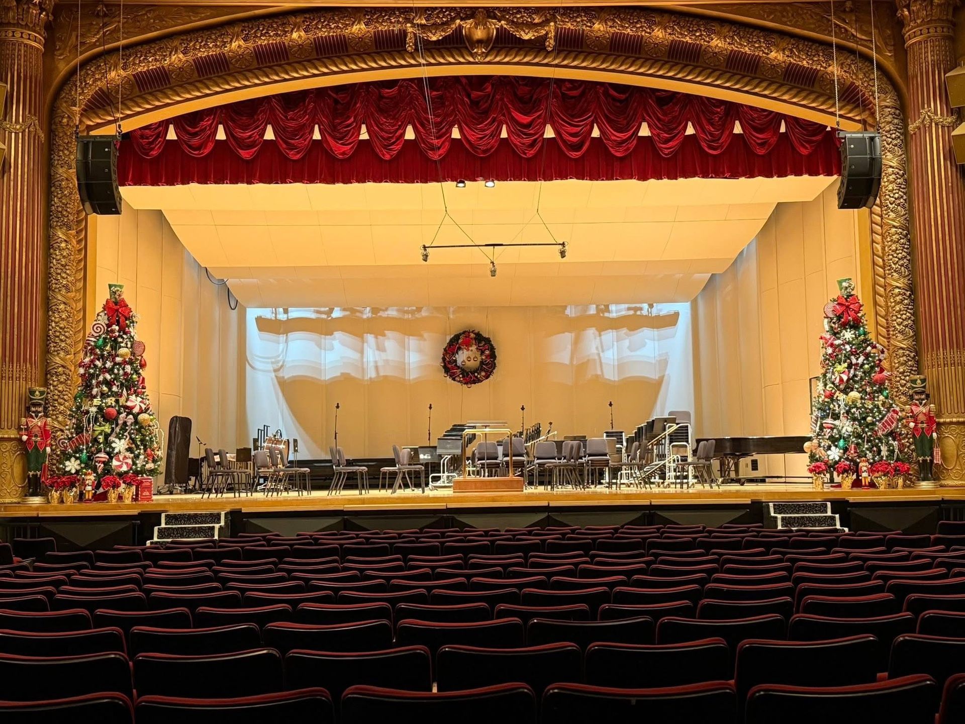 Decorated theater stage with red curtains, Christmas trees, and empty orchestra seats
