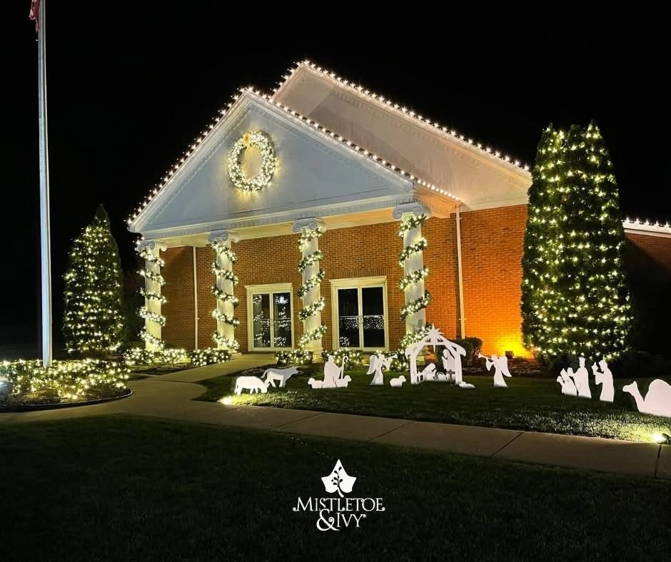 Brick building decorated with white holiday lights and Christmas trees at night.
