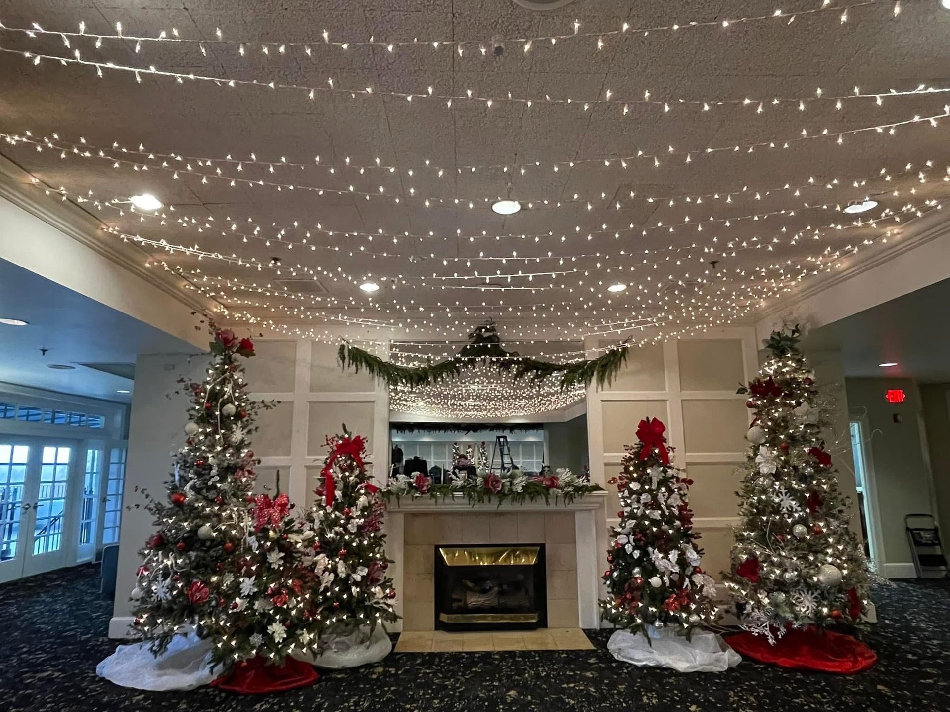 Festive lobby with lit Christmas trees, garland, and twinkle lights above a fireplace