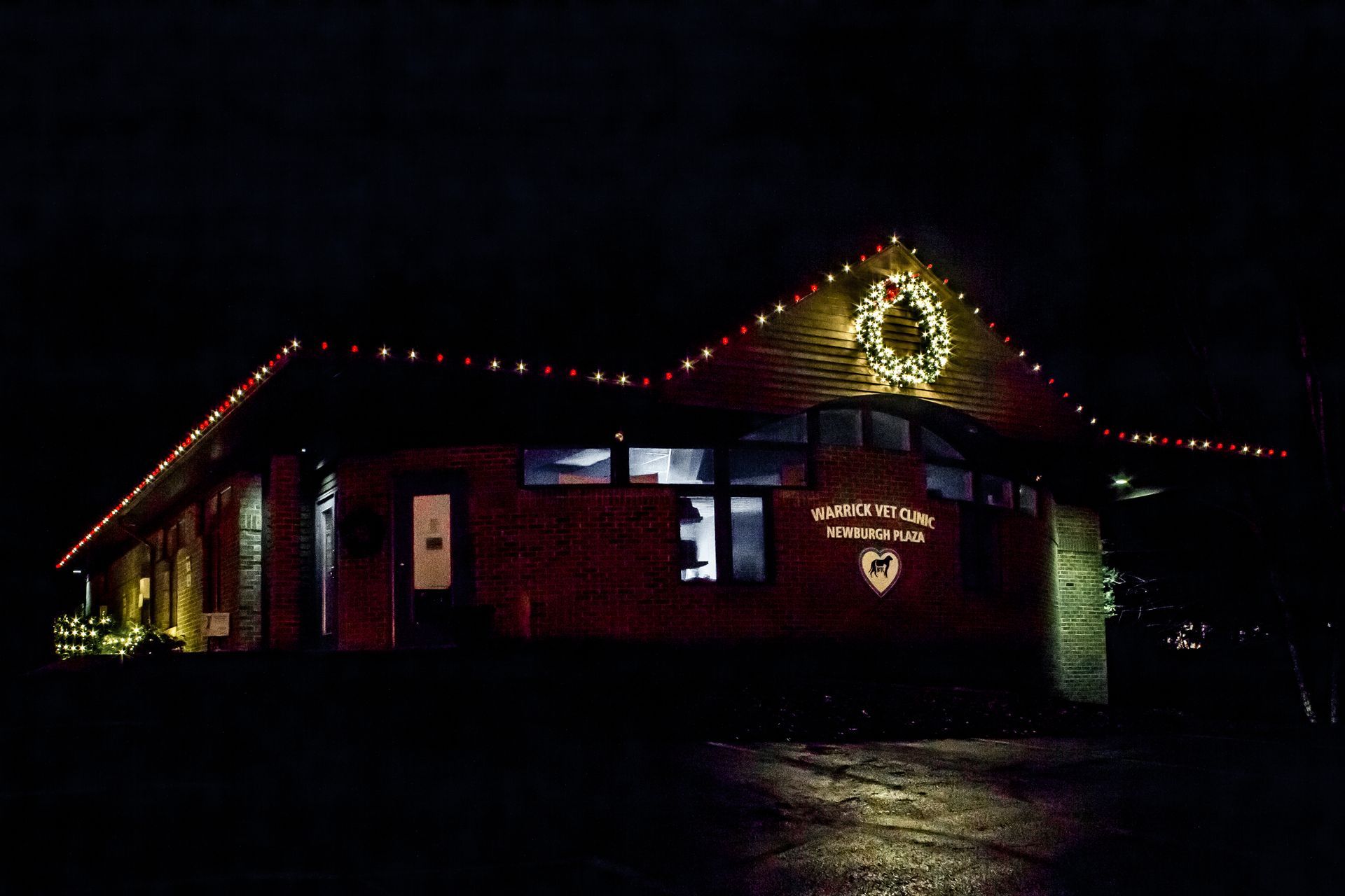 Red brick building at night with red roof lights and a lit Christmas tree sign on the front