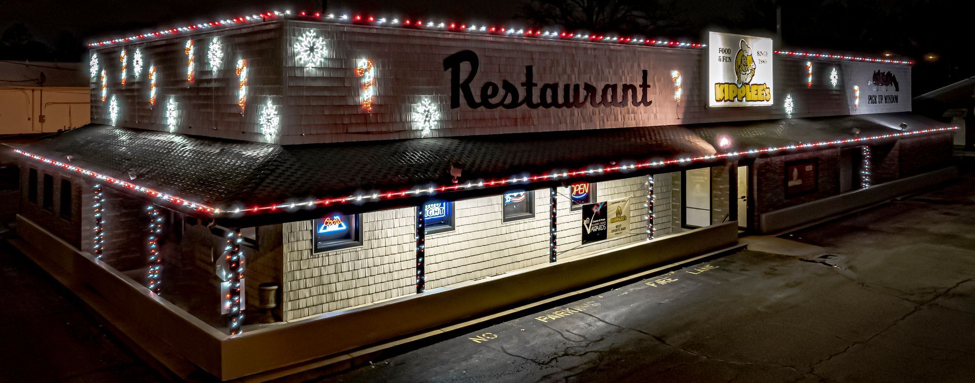 Night view of a lit restaurant building with red trim and snow along the roofline