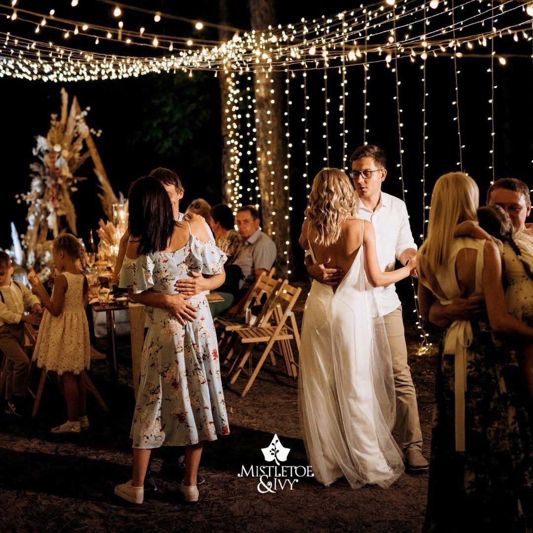 People dancing at an outdoor nighttime party, under string lights.