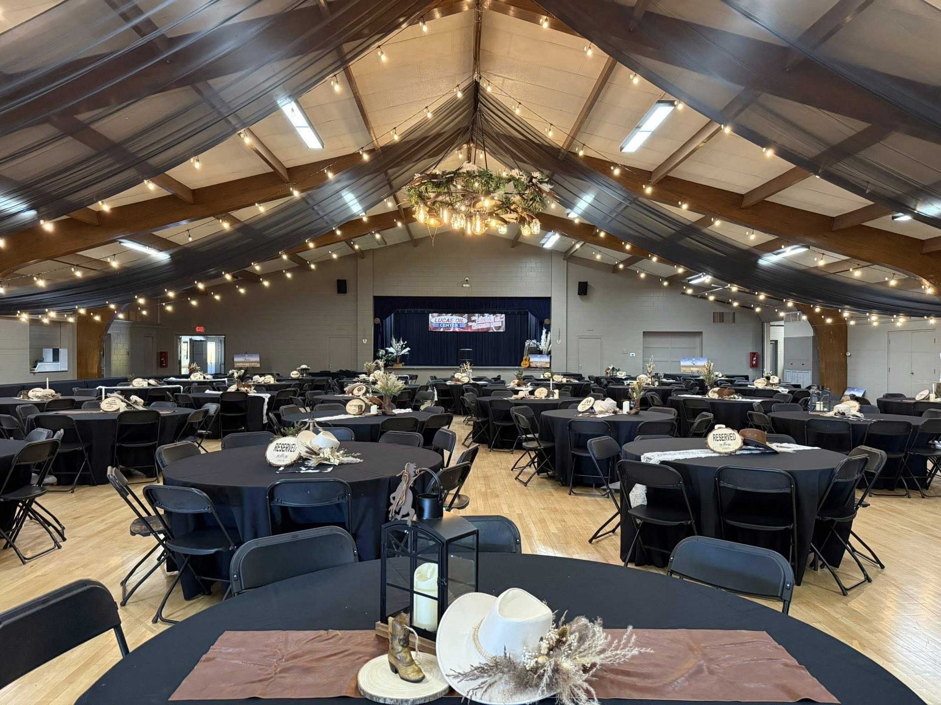Reception hall with round tables covered in black linens, set for an event; decorative lights.