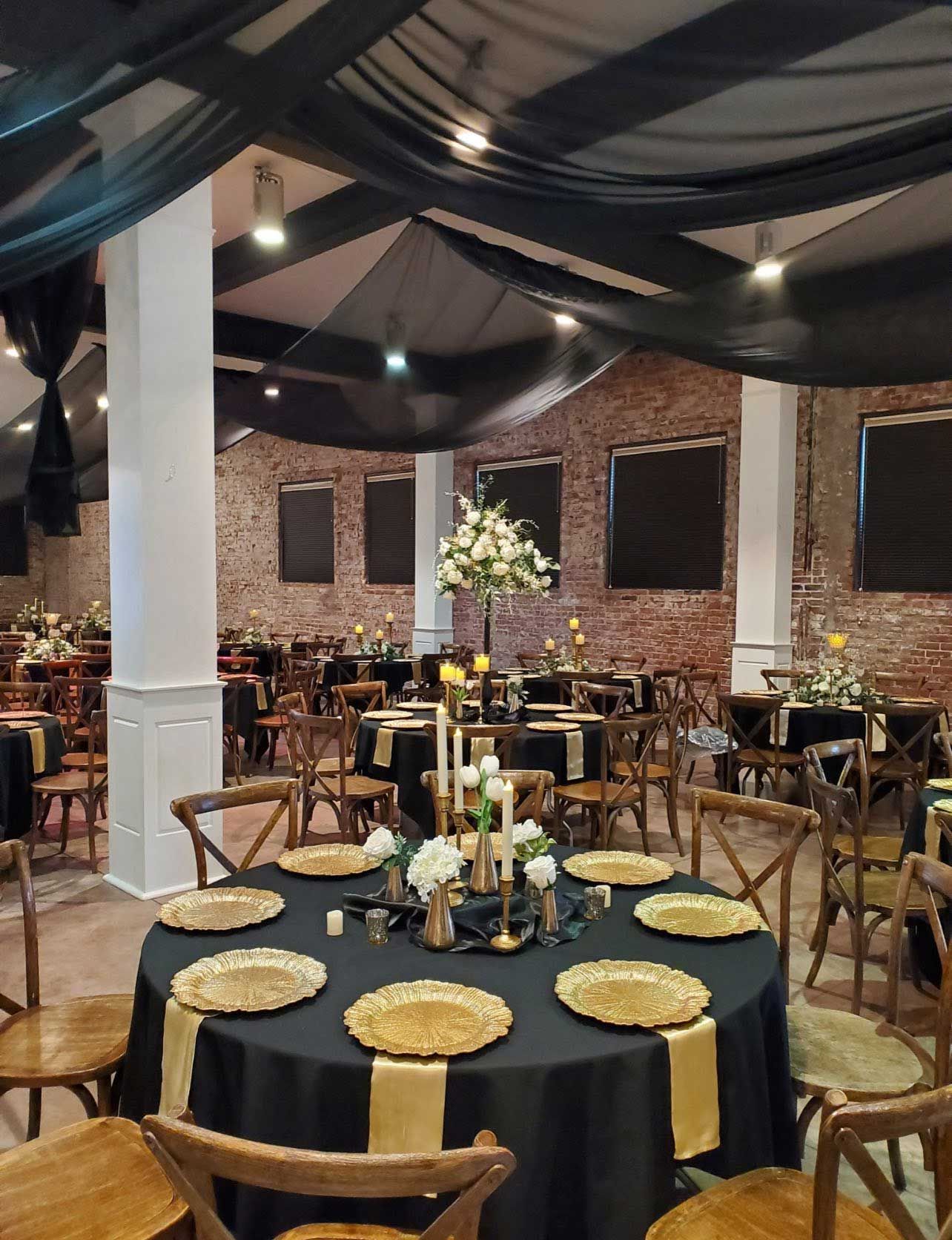 Formal event space with round tables, black linens, gold accents, and floral centerpieces.