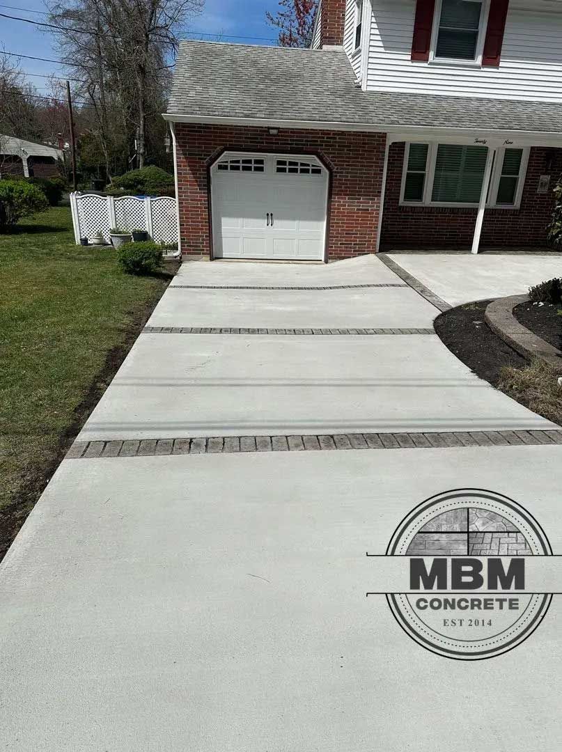 Concrete driveway with brick borders leading to a garage in front of a house.