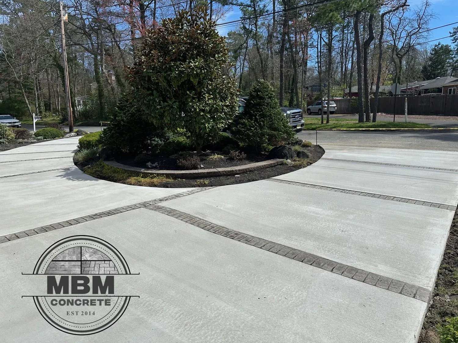 Concrete driveway with a landscaped island, bordered with brick. MBM Concrete logo visible.