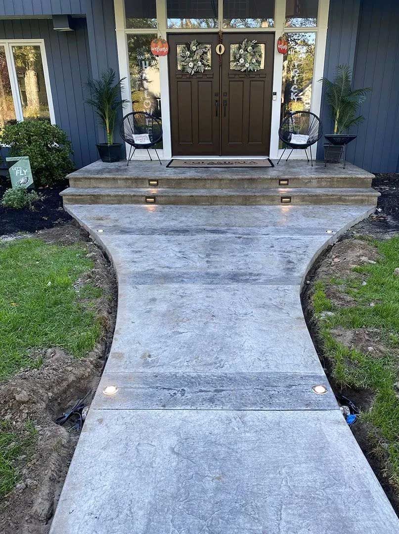Gray concrete walkway leading to a front door with steps. Two potted plants sit beside the door.