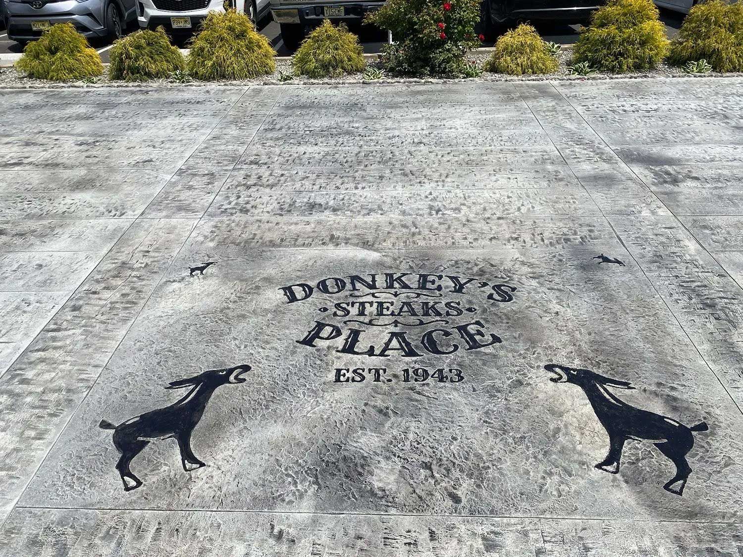 Donkey's Steaks + Place logo on a concrete surface, flanked by dog silhouettes. 