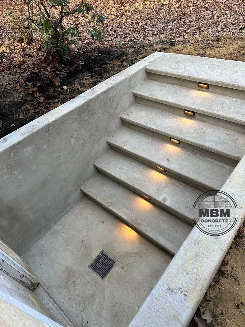 Concrete stairs descend into a recessed area, lit by embedded lights.
