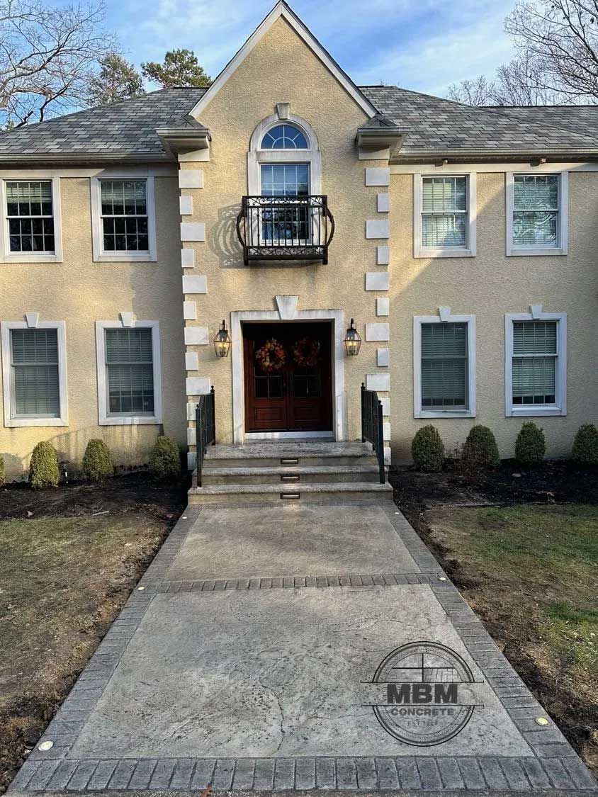 Two-story beige house with brown door, a stone walkway, and a decorative balcony.