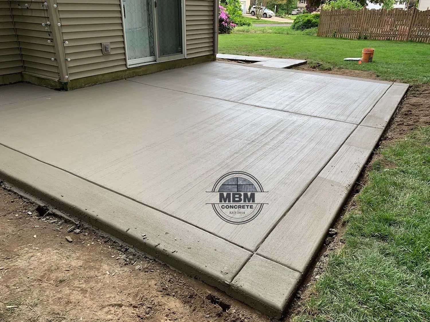 Newly poured concrete patio with a textured finish next to a house.