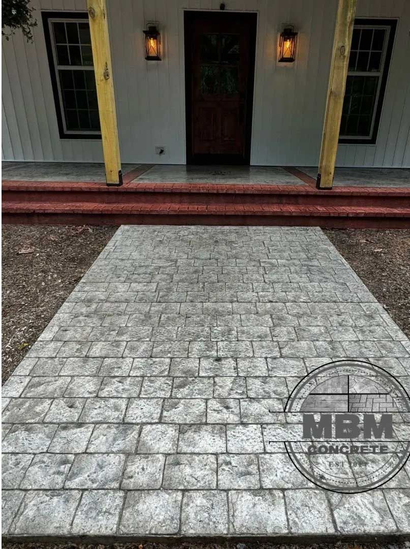 Stamped concrete walkway leading to a house's front door, with brick pattern, gray color.