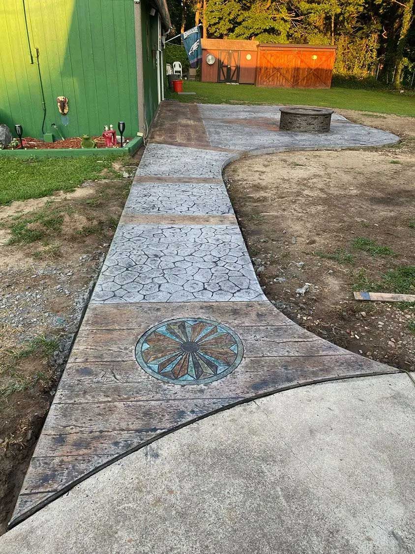 Concrete walkway with decorative stamps and a fire pit in a backyard.