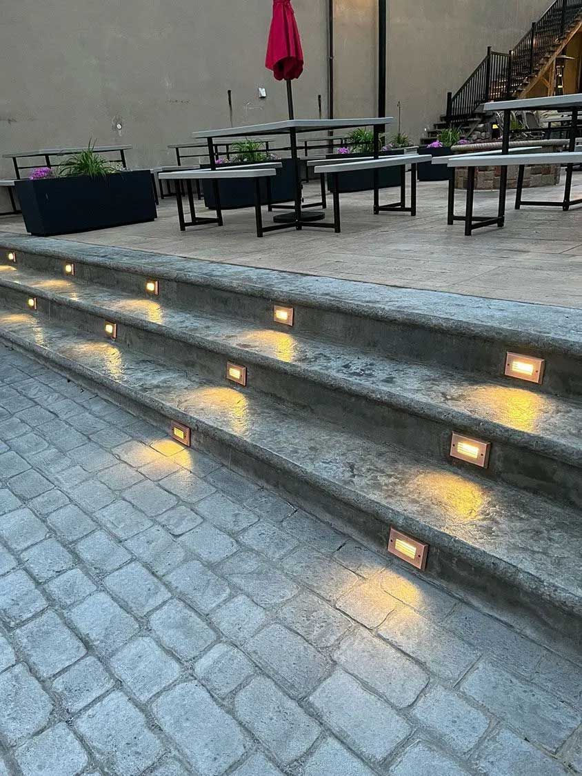 Outdoor steps with inset lights leading to a patio with tables and an umbrella.