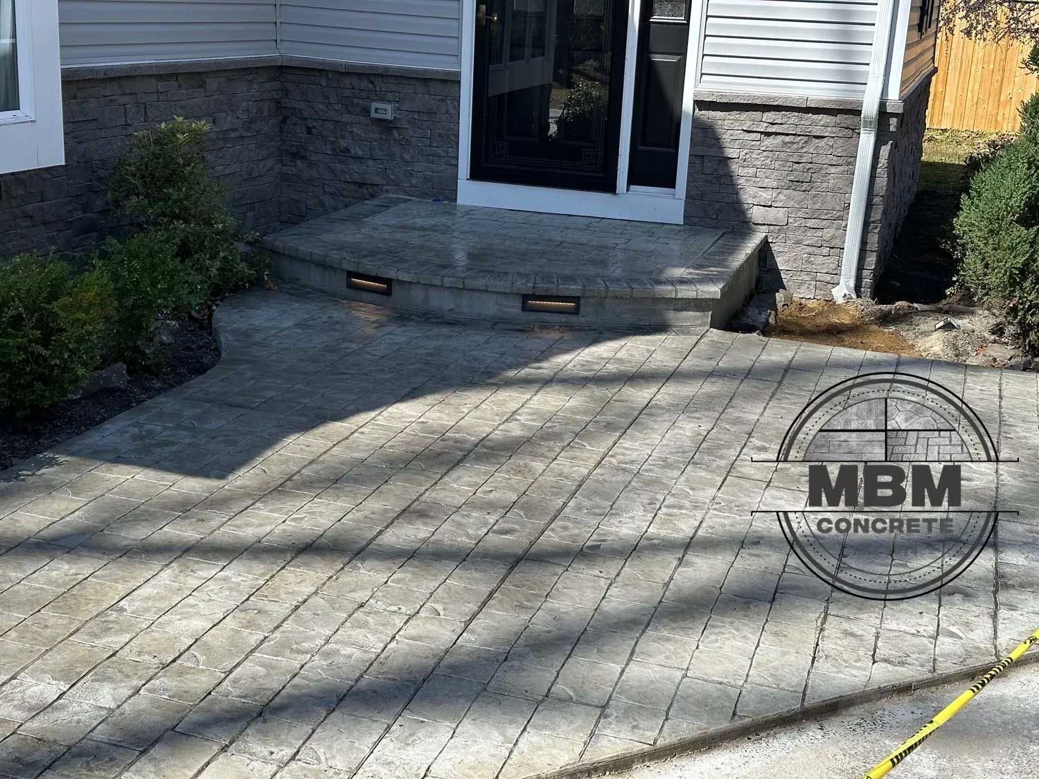 Concrete patio with steps leading to a doorway. Textured pavers in a light gray color.