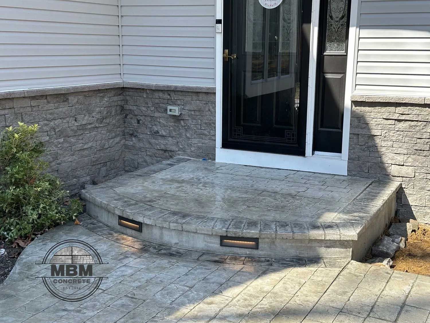 Front entry with stone facade, concrete steps, and a black door.