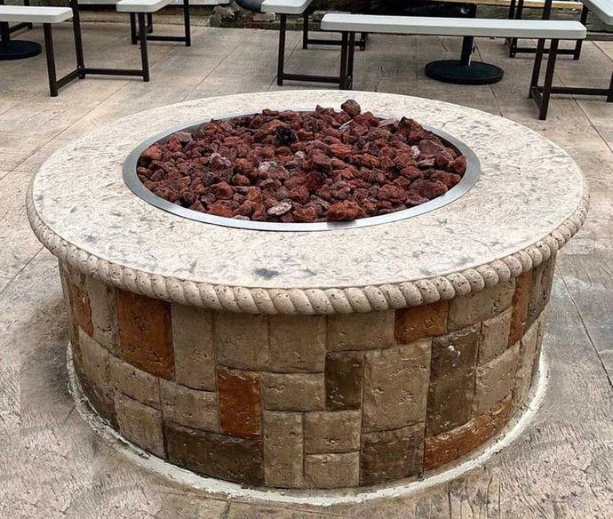 Circular stone fire pit with brown lava rocks, surrounded by outdoor seating.