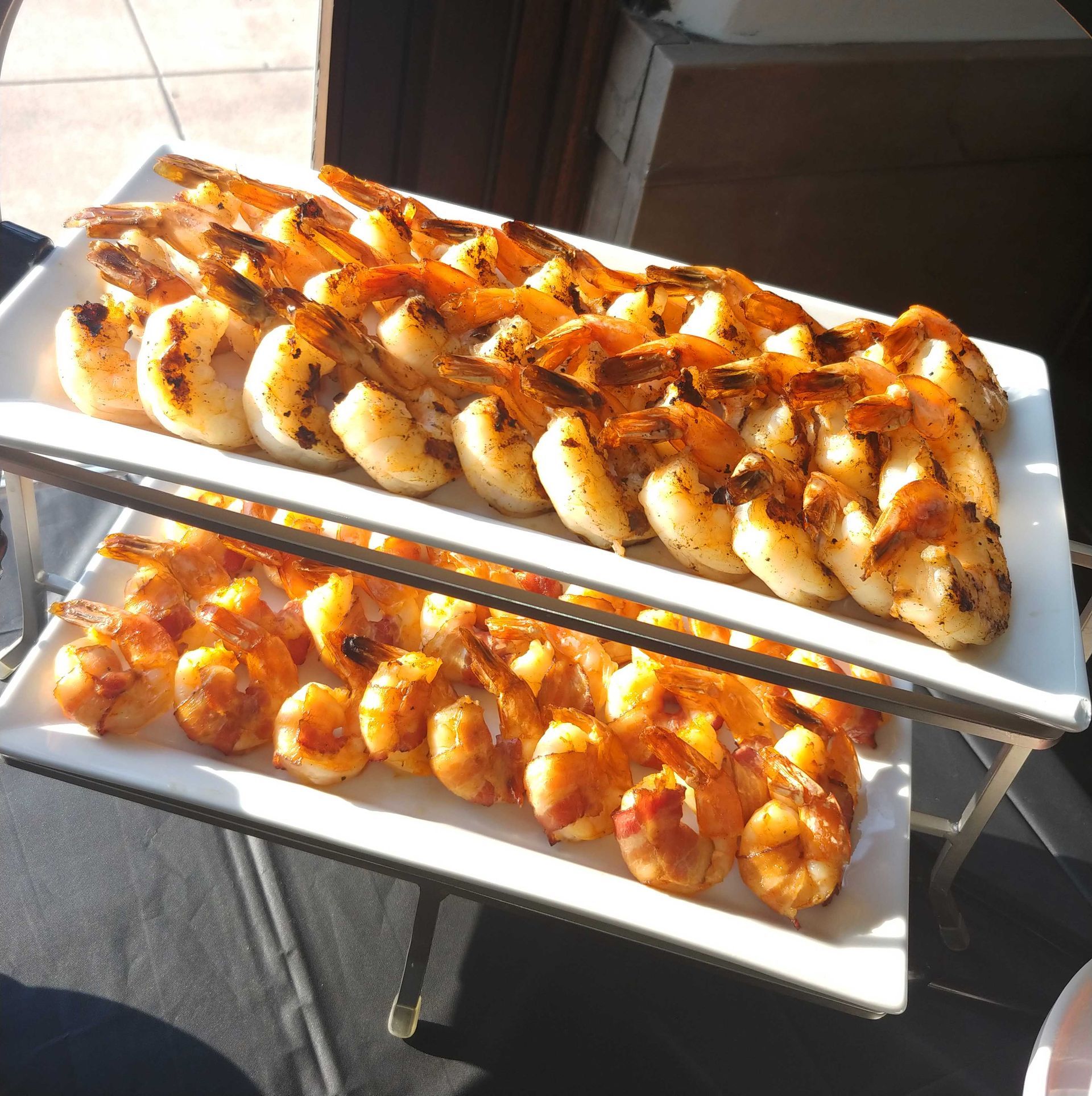 Grilled shrimp on white platters, arranged on a tiered serving stand, outdoors.