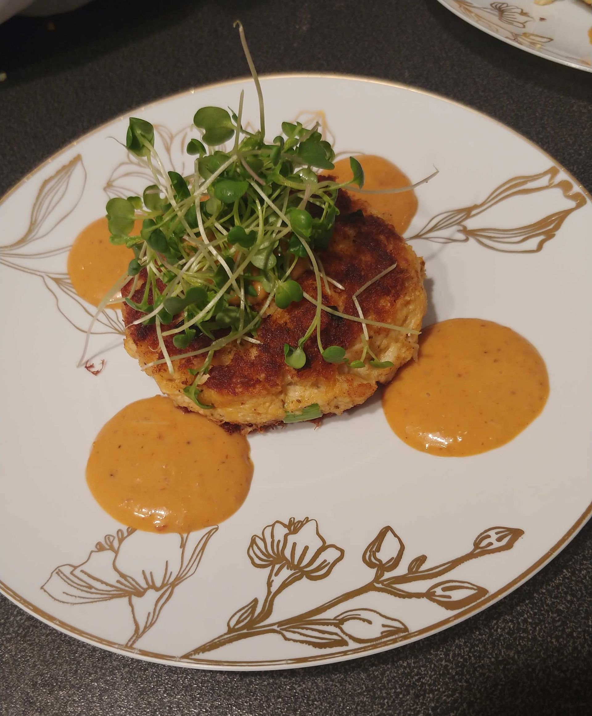 Crab cake with sauce and microgreens on a decorative plate.