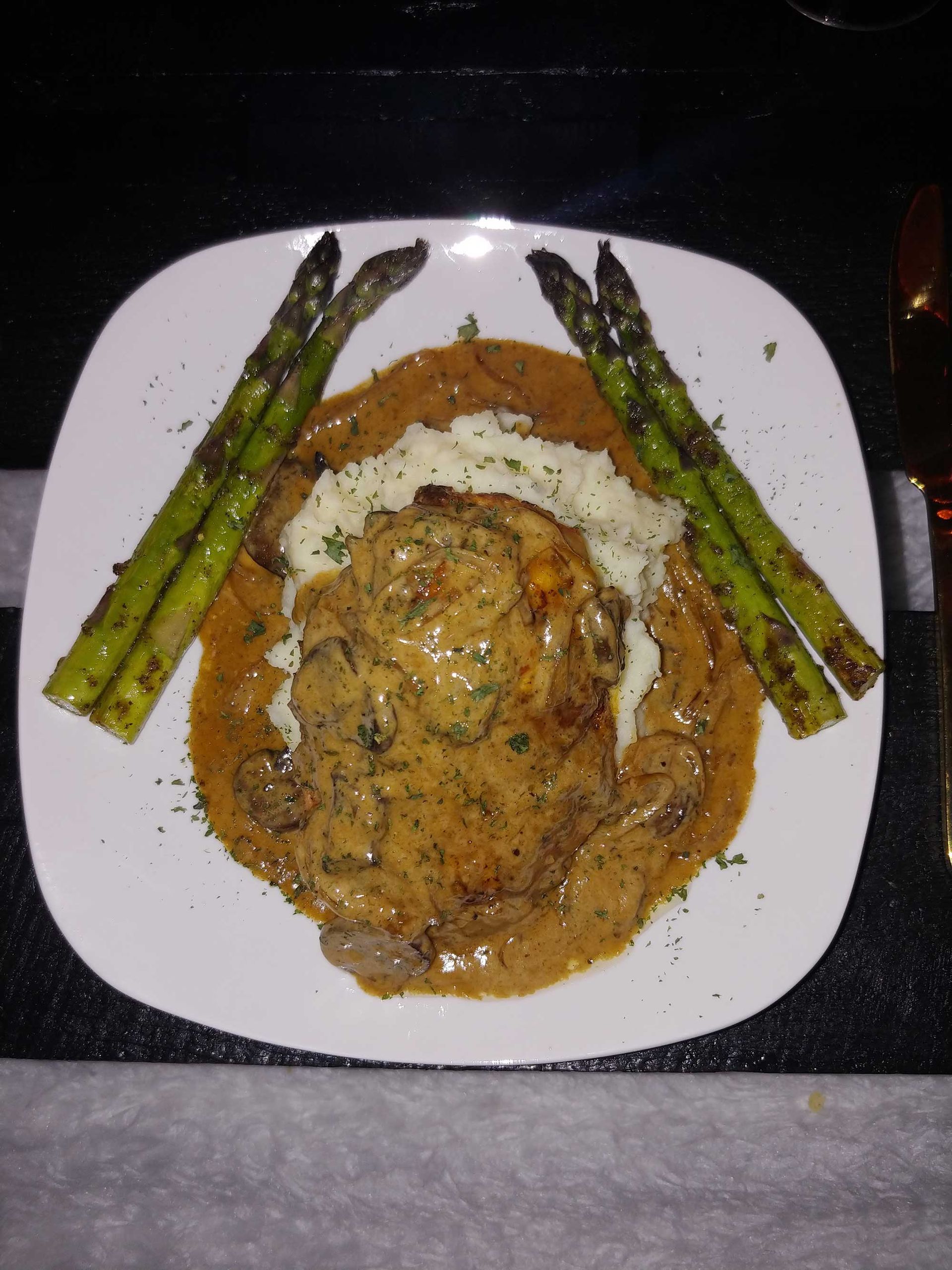 Chicken dish on a white plate with asparagus, creamy sauce, and mashed potatoes.