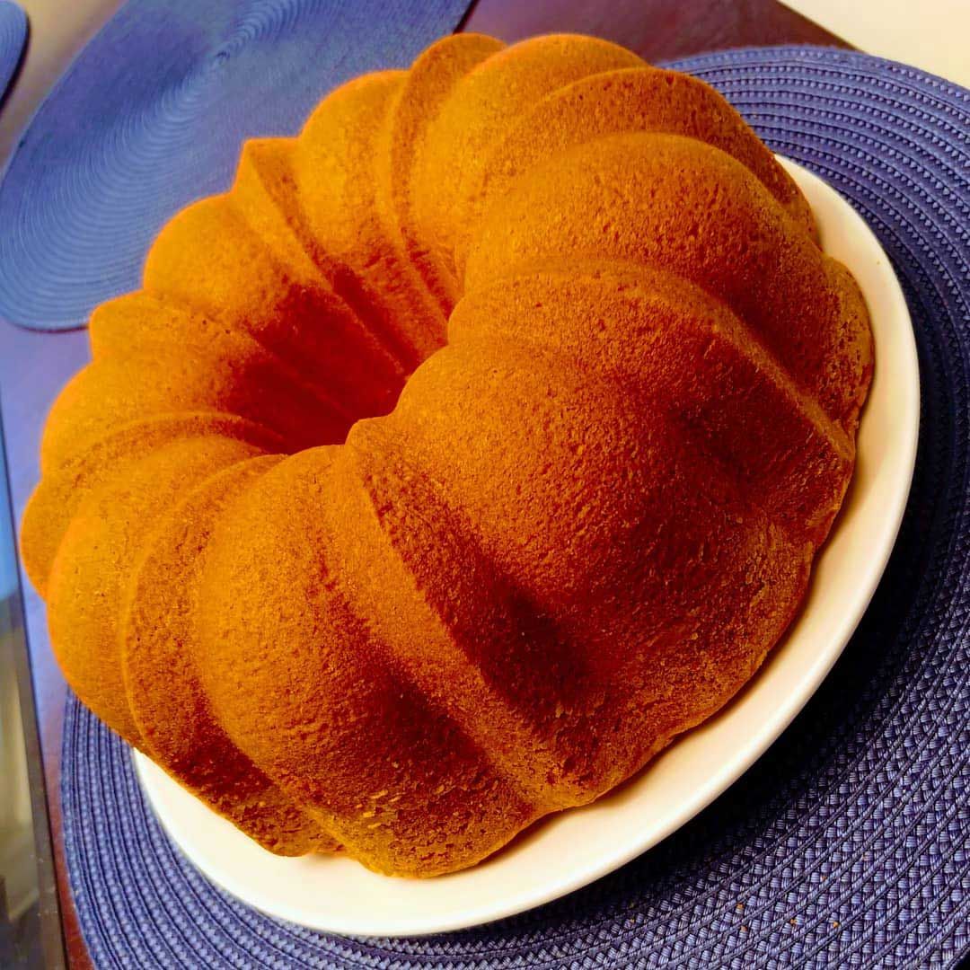 Golden-brown bundt cake on a white plate, set on a blue placemat.