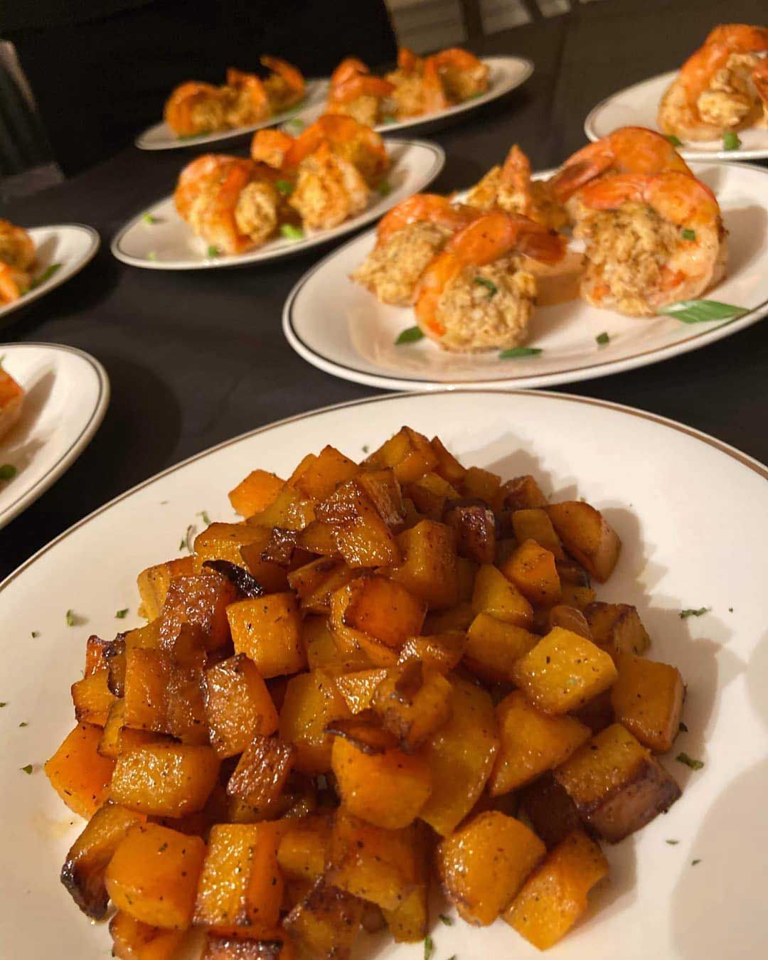 Plates of roasted butternut squash and stuffed shrimp on a black tablecloth.