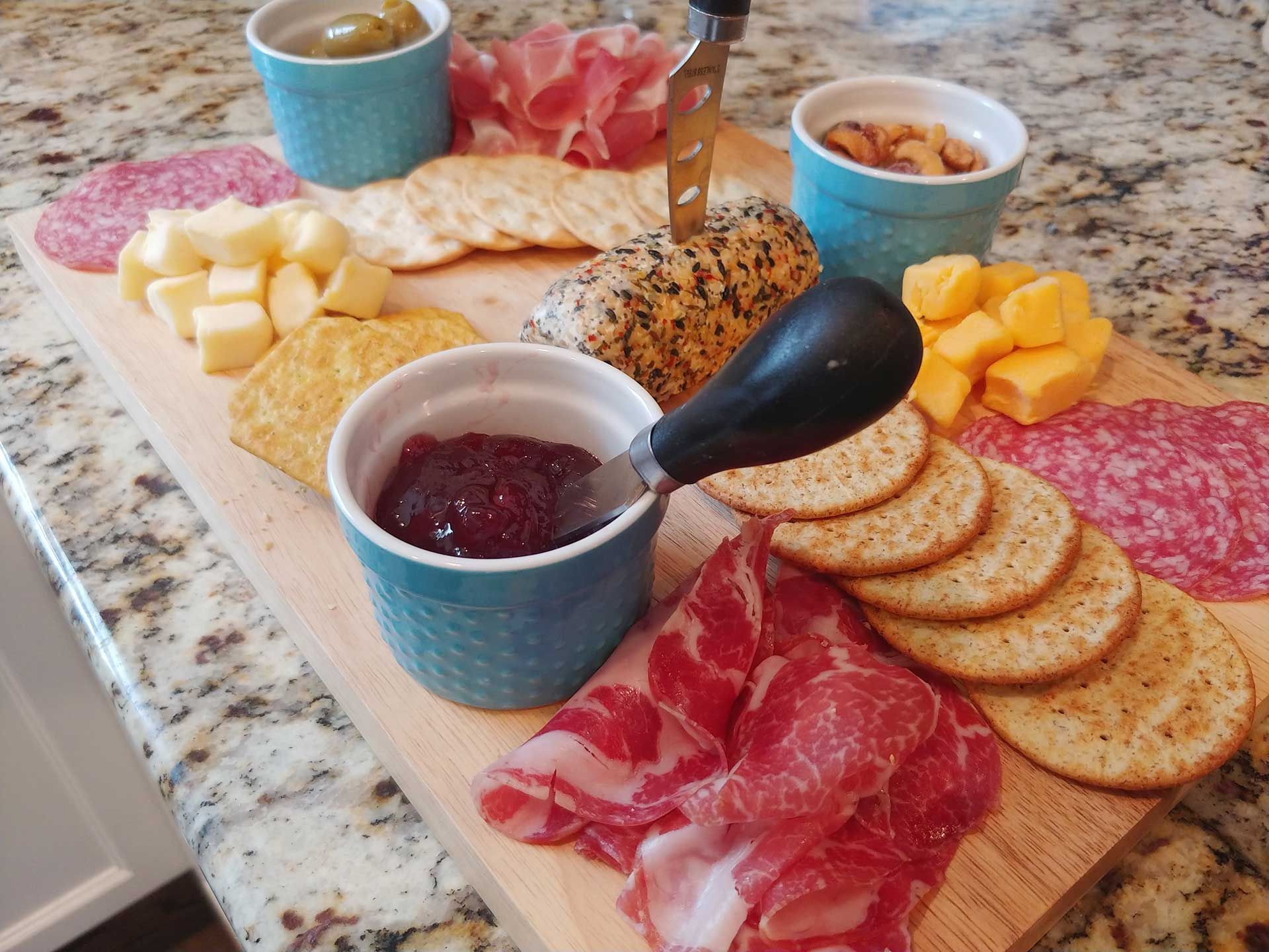 Charcuterie board with meats, cheeses, crackers, nuts, and jam.