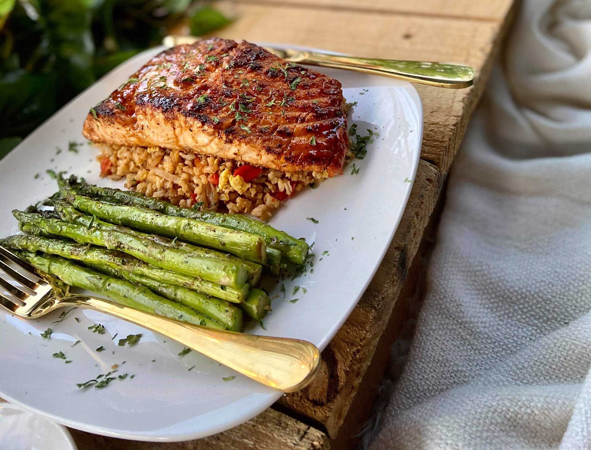 Grilled salmon over grains, with asparagus and a gold fork on a white plate.