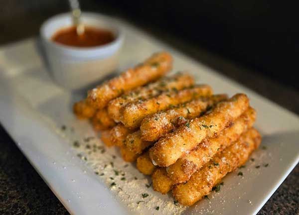Golden-brown mozzarella sticks piled on a white plate with marinara sauce.