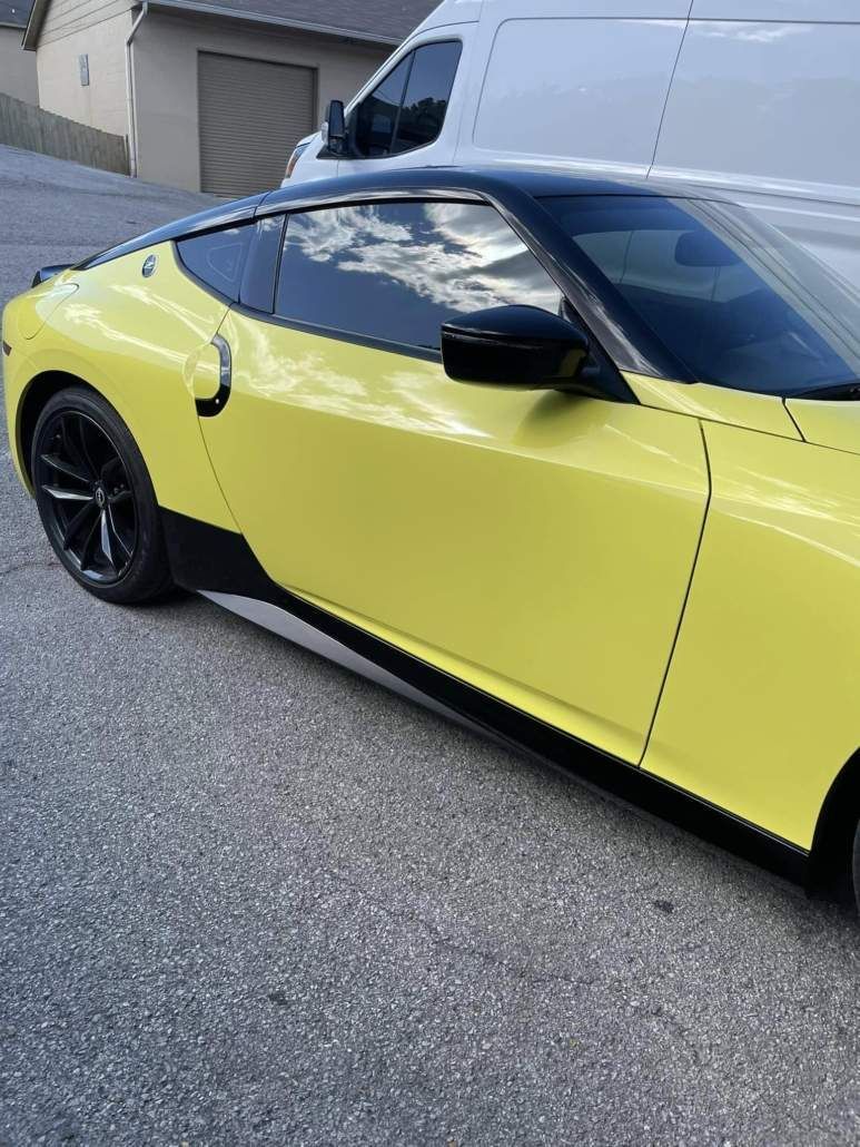 Yellow and black sports car on asphalt; black wheels, roof, and trim; cloudy sky reflection in window.