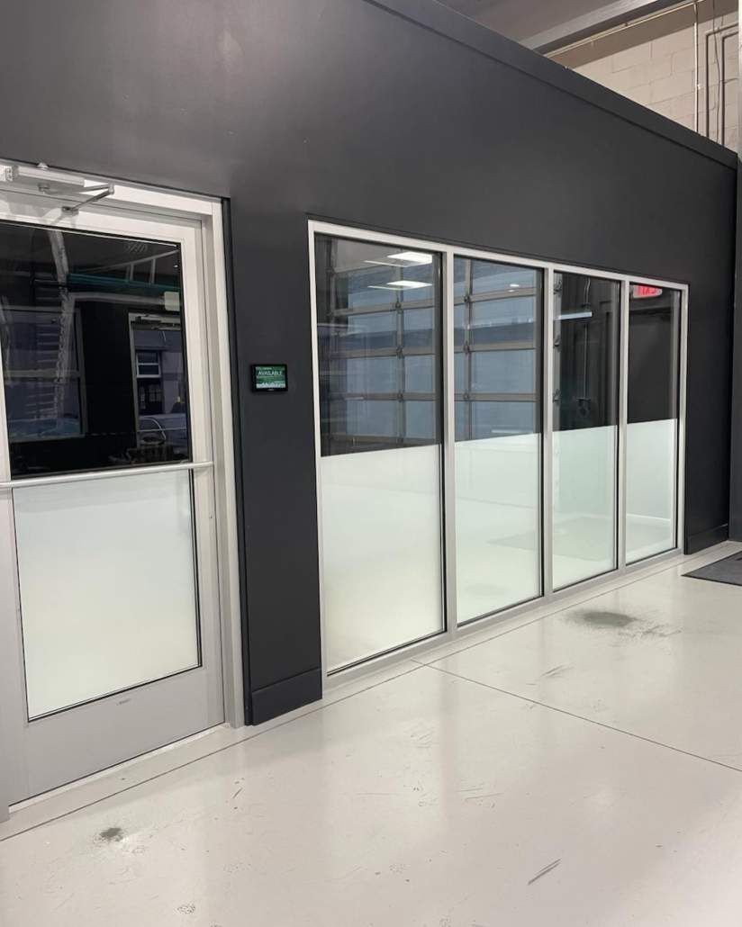 Exterior of a building with a door and large windows, frosted at the bottom, gray walls, white floor.