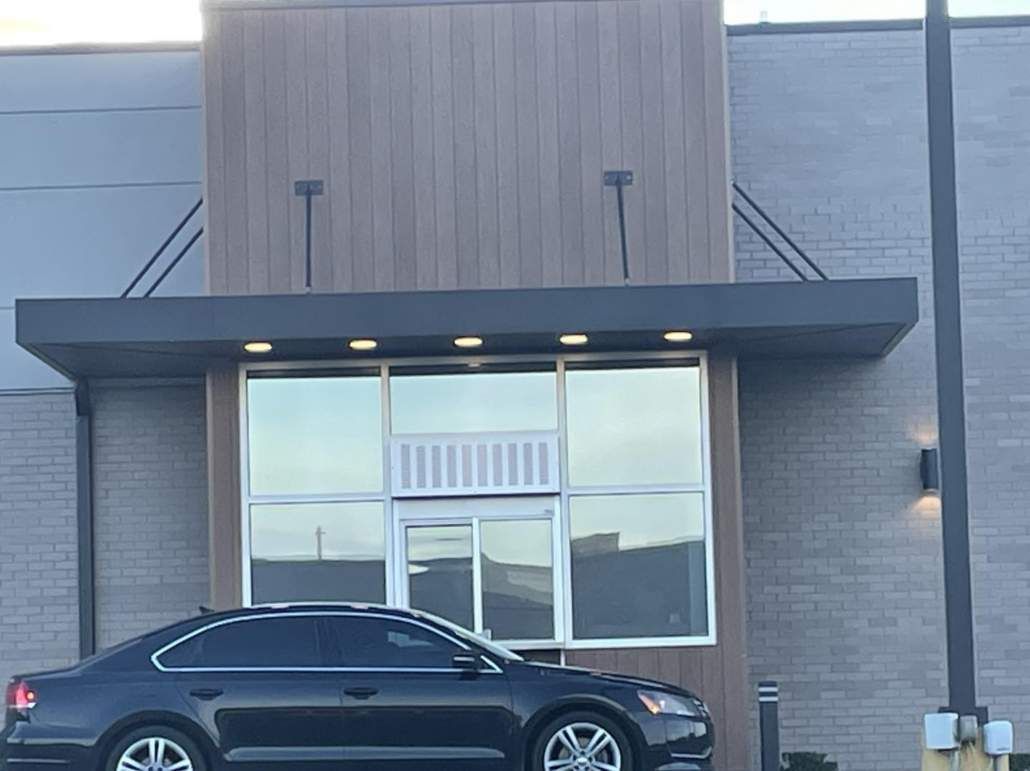 Dark sedan parked in front of a modern building with large windows and a dark overhang.