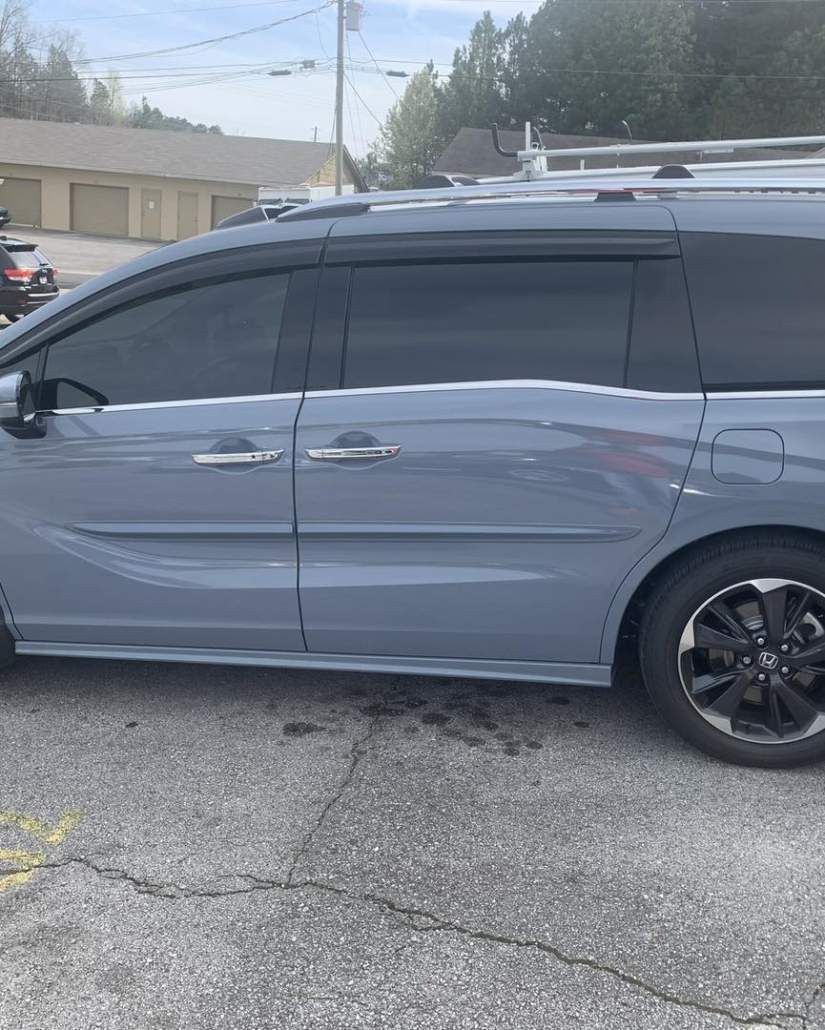 Gray minivan parked outdoors, tinted windows, black wheels, overcast sky.