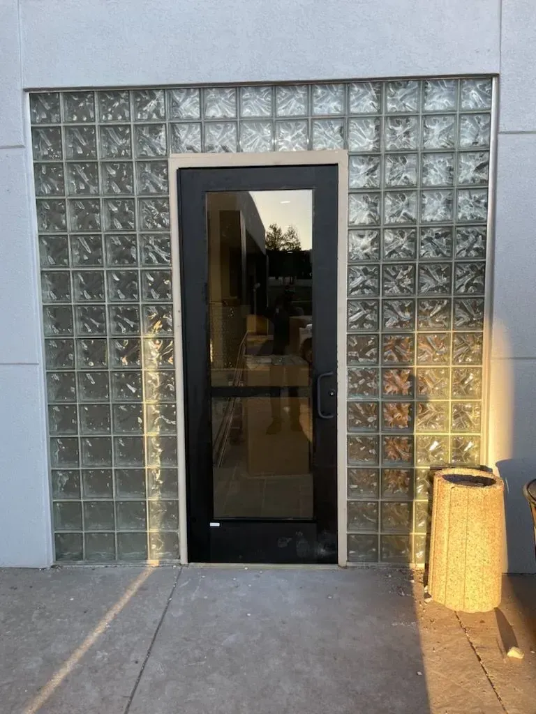 Glass-block wall with a black-framed glass door and a lit lantern beside the entrance.