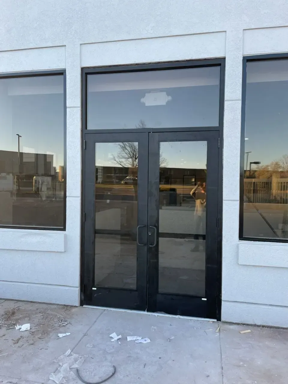 Black double glass storefront door flanked by large windows on a plain white building exterior.